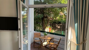 Varanda com mesa e cadeiras de madeira, um vaso de planta e vista para árvores e uma cerca.