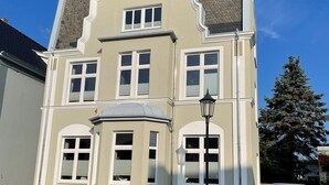 Un immeuble de deux étages avec une façade blanche, de nombreuses fenêtres et un petit balcon.