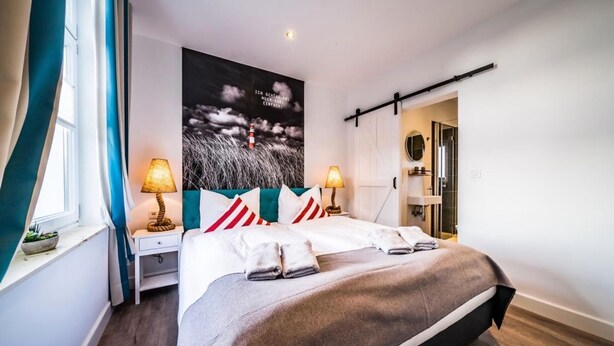 Une chambre moderne avec un grand lit, deux tables de chevet avec des lampes, une étagère murale et une porte donnant sur une salle de bain.