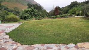 Ein angelegter Garten mit einem Kiesweg, der zu einer Rasenfläche führt, umgeben von Bäumen und einem Berg im Hintergrund.