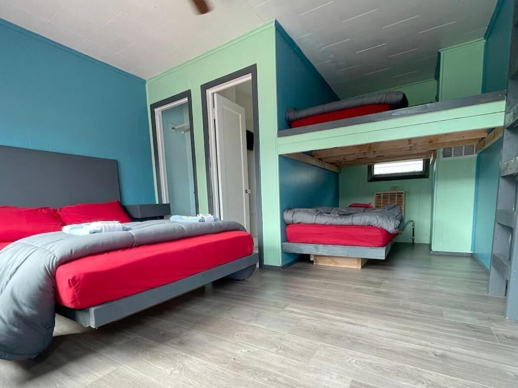 Une chambre avec deux lits, dont un au sol et l’autre dans un lit superposé, avec des murs de couleur turquoise et un plancher en bois.