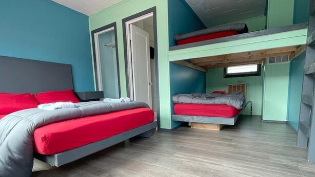 A room with two beds, one on the floor and one on a bunk bed, with teal walls and wooden flooring.
