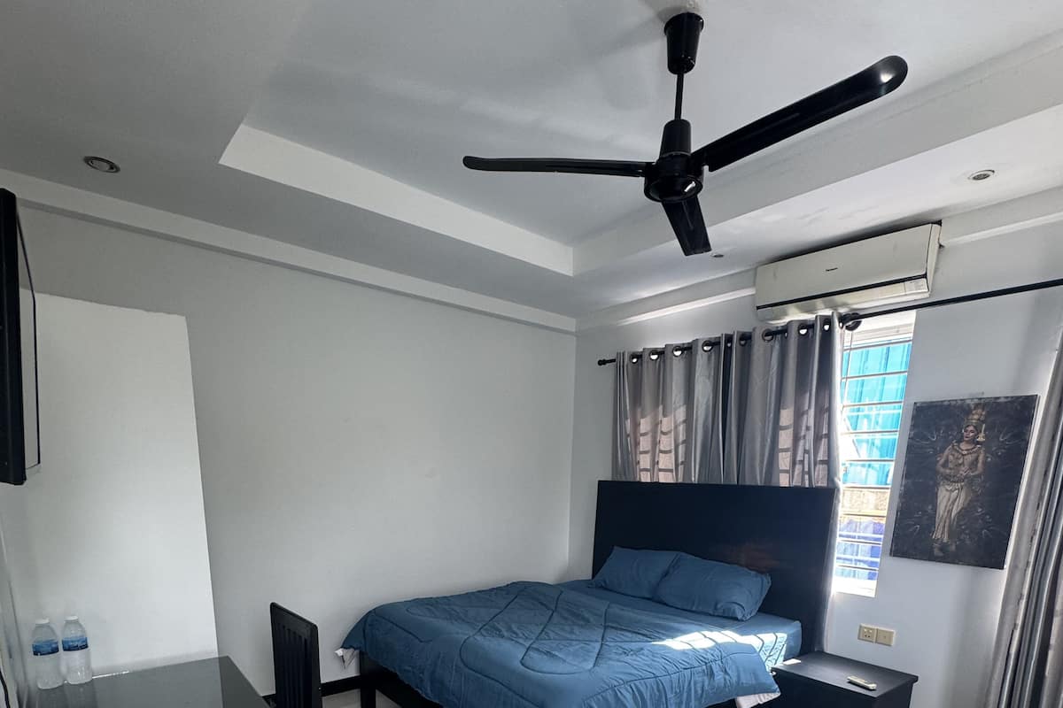 Un dormitorio moderno con cama, escritorio, ventilador de techo y ventana con cortinas.