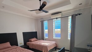 Quarto de hotel com duas camas, uma escrivaninha e um ventilador de teto.