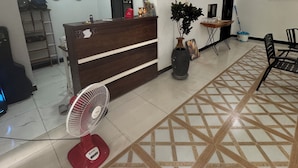 Uma área de recepção com balcão de madeira, um ventilador e piso de azulejos com padrão geométrico.