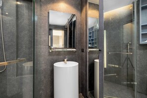 A modern bathroom with a large mirror, a white sink, and a glass shower enclosure. - Condo with Full Facilities C255 (Kamala)