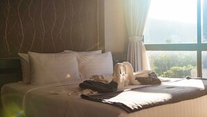 A hotel room with a bed, pillows, a blanket, and a window with a view of greenery. - Condo with Full Facilities C255 (Kamala)