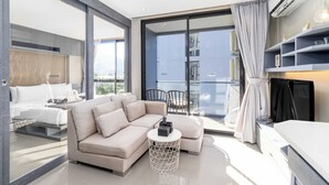 A modern hotel room with a sofa, a small round table, a TV, and a balcony with a view of the city. - Condo with Full Facilities C255 (Kamala)