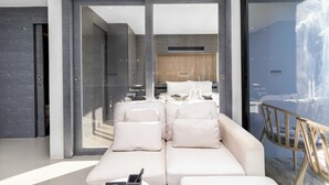 A modern interior with a sofa, a wooden chair, and a glass door leading to a bedroom. - Condo with Full Facilities C255 (Kamala)