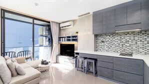 A modern living room with a sofa, a TV, and a balcony with chairs. - Condo with Full Facilities C255 (Kamala)