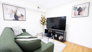 Ein Wohnzimmer mit einem grünen Sofa, einem Flachbildfernseher, einem Glastisch und einer Vase mit Blumen.