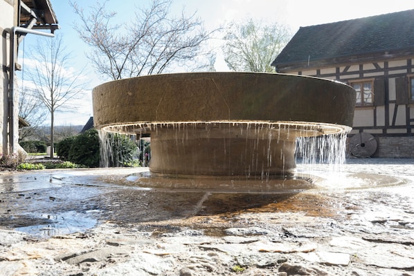 A stone fountain with water spouting from its center, surrounded by a stone-paved area.