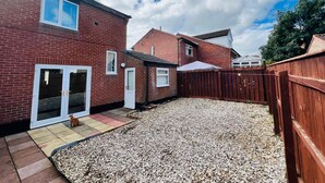 A residential backyard with a gravel patio, a wooden fence, and a brick house. - Modern Comfortable Two Bedrooms House DL5 With Garden Parking and Free Wifi (Newton Aycliffe)