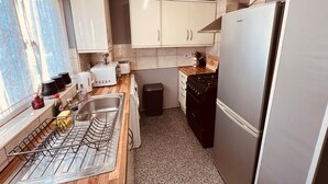 A compact kitchen with white cabinets, a stainless steel refrigerator, a gas stove, and a sink with a drying rack. - Modern Comfortable Two Bedrooms House DL5 With Garden Parking and Free Wifi (Newton Aycliffe)