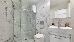 Une salle de bain moderne avec une douche à parois de verre, des toilettes blanches et un meuble-lavabo doté d’un miroir et d’un évier.