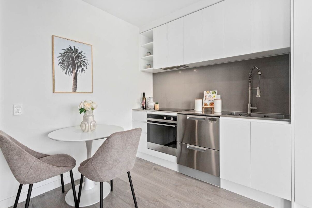 A modern kitchen with white cabinets, stainless steel appliances, and a white dining table with two chairs.