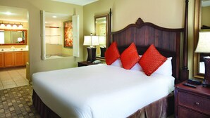 Ein Hotelzimmer mit einem großen Bett, einem Holzkopfteil, einem Nachttisch, einem Spiegel und einem Deckenventilator.