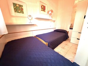 Una habitación pequeña y funcional con dos camas individuales, un estante con espejo y un armario blanco.