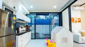 A modern kitchen with a refrigerator, cabinets, and a dining area with a white table and chairs. - Emery Pool Villa Pattaya
We are welcome your family,friend and your pet (Banglamung)