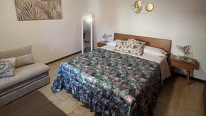 A bedroom with a bed, a nightstand, a bedside lamp, a sofa, and a wall-mounted light fixture. - The House of Anastasia (Taino)