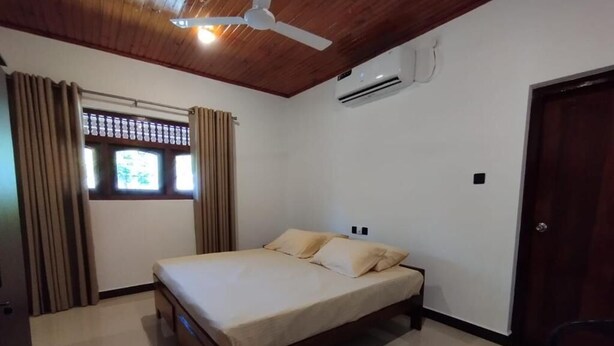 Un dormitorio con cama, ventilador de techo, equipo de aire acondicionado, ventana con cortinas y puerta.