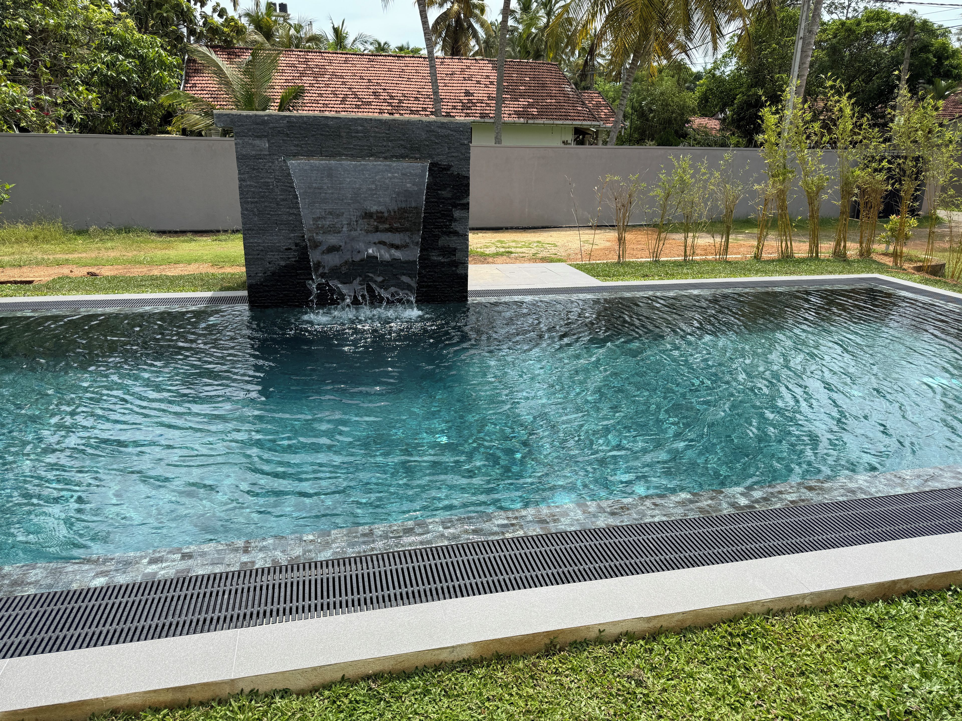 Una piscina rectangular con un elemento central de agua y un área verde circundante.