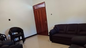 Una sala de estar con un sofá oscuro, una pequeña silla negra y una puerta de madera.