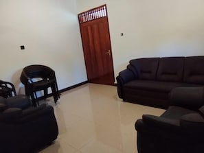 Una sala de estar con un sofá oscuro, una pequeña silla negra y una puerta de madera.