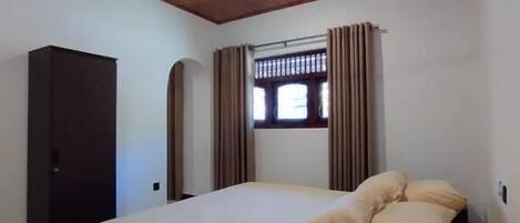 A bedroom with a bed, a ceiling fan, a window with curtains, and a wardrobe.