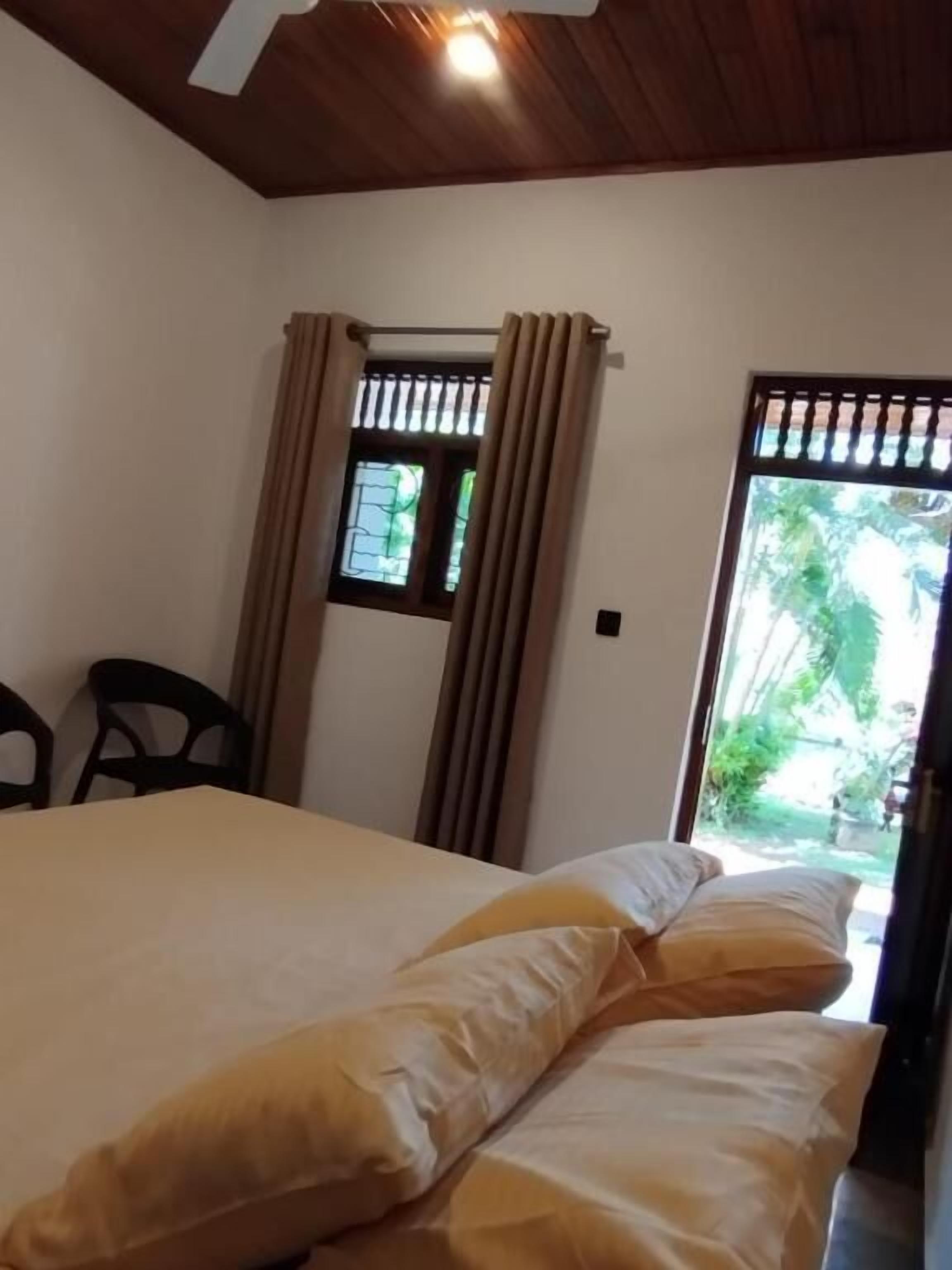 Una habitación con cama, ventana con cortinas y vistas al exterior con vegetación.