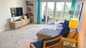 Uma sala de estar com sofá, poltrona, televisão e estante de livros.