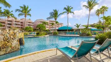 A swimming pool with lounge chairs, palm trees, and a building with balconies.