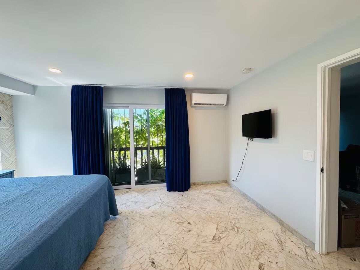 A hotel room with a bed, a TV, and a sliding glass door leading to an outdoor area.