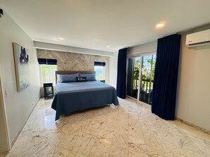 A modern bedroom with a large bed, a herringbone-patterned wall, and a view through a glass door.
