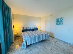 A hotel room with a bed, two bedside lamps, a door, a wall art piece, and a marble floor. - St Thomas 2BR Oceanside Villa with Views: Steps to Beach, Pool & Restaurants (Charlotte Amalie)