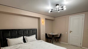 Un dormitorio con una cama grande, una mesita con dos sillas, una puerta y una lámpara en el techo.