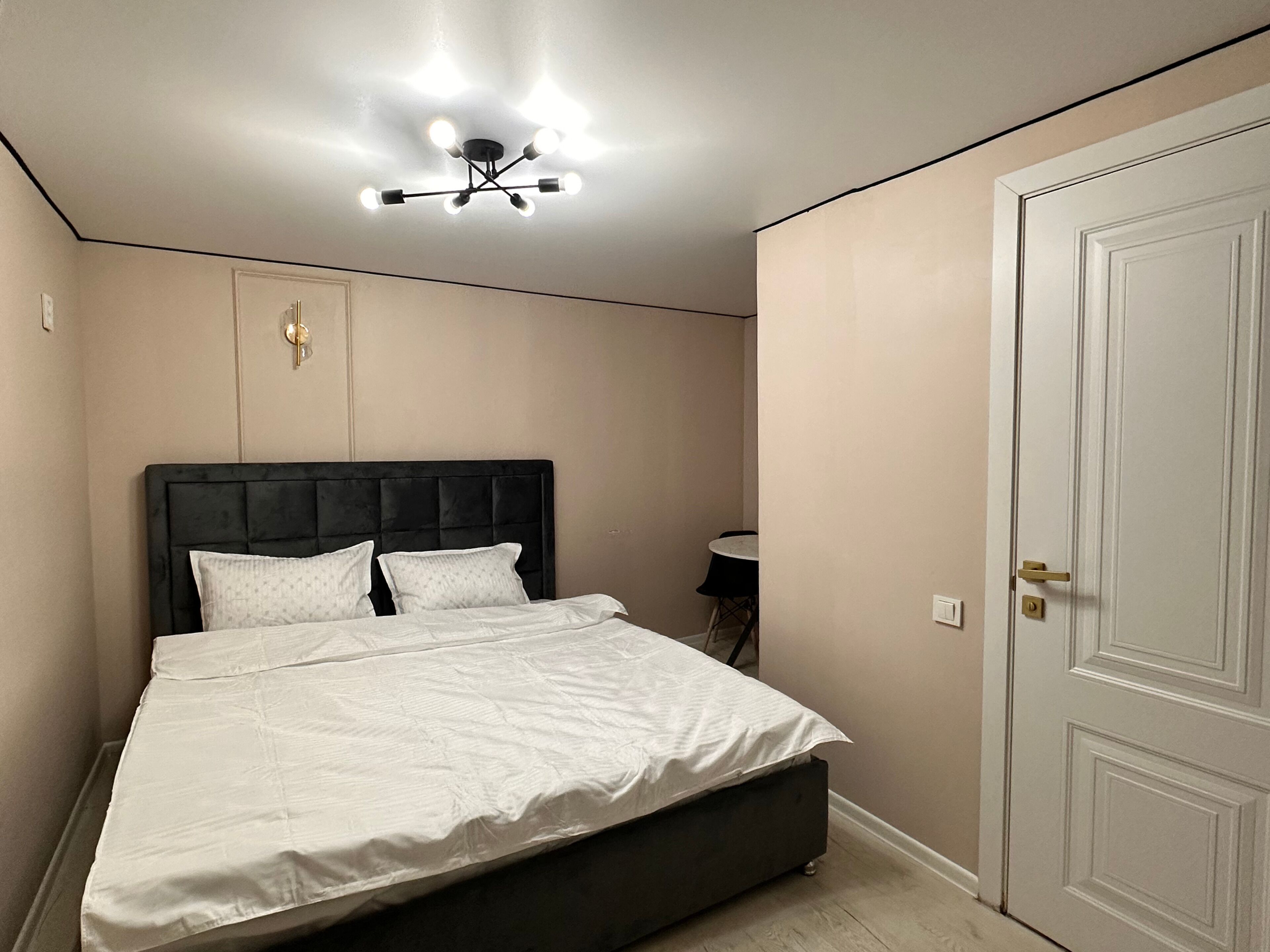 Ein Schlafzimmer mit einem Bett, einer Deckenleuchte, einer Tür und einem kleinen Tisch.