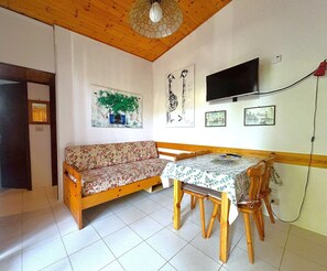 Een kamer met een houten plafond, een bank, een eettafel met stoelen, een aan de muur bevestigde televisie en kunstwerken op de wanden.