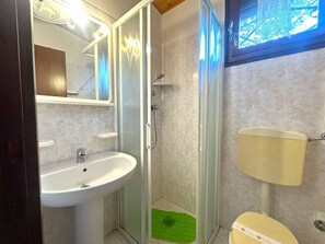 Een badkamer met een douche met glazen wanden, een witte wastafel en een toilet.