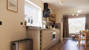 A modern kitchen with a built-in oven, a compact refrigerator, and a dining area with a table and chairs. -  Cosy Cottage with sea view, 10 mins from Portree (Portree)