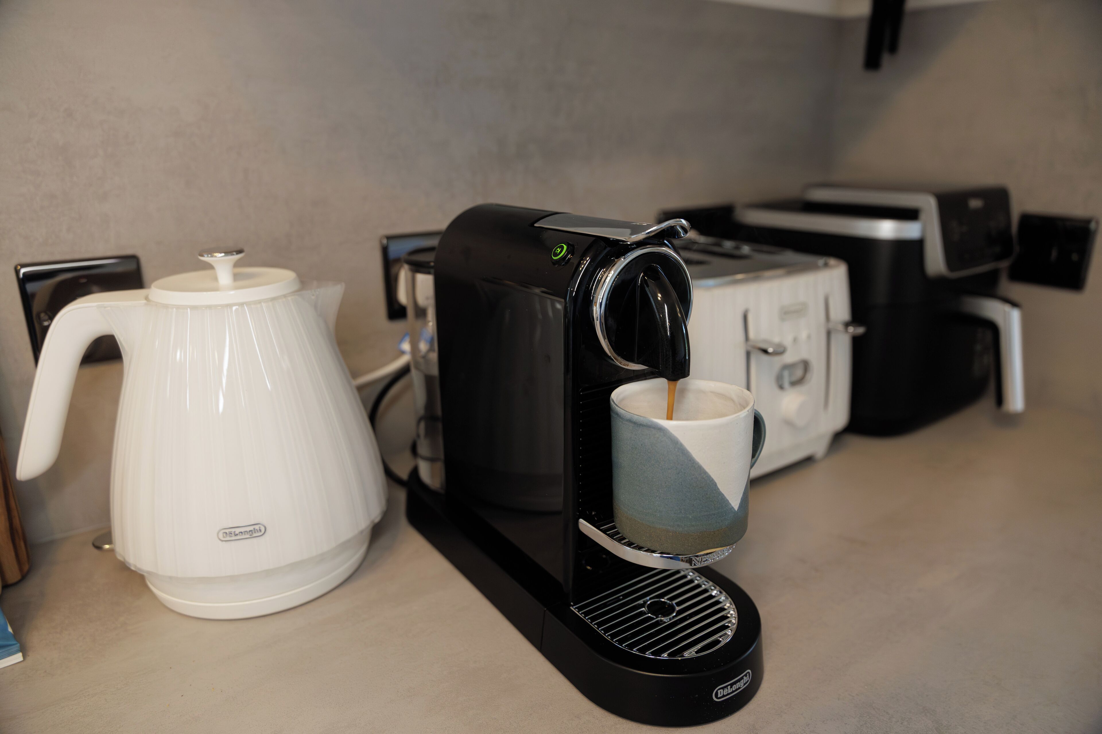 Una cafetera, un tostador y una tetera sobre una encimera.