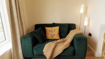 A green sofa with a throw blanket, a yellow pillow with a dog design, and a floor lamp.