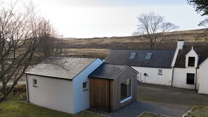A modern house with a sloped roof, a small wooden shed, and a white building with a chimney. -  Cosy Cottage with sea view, 10 mins from Portree (Portree)