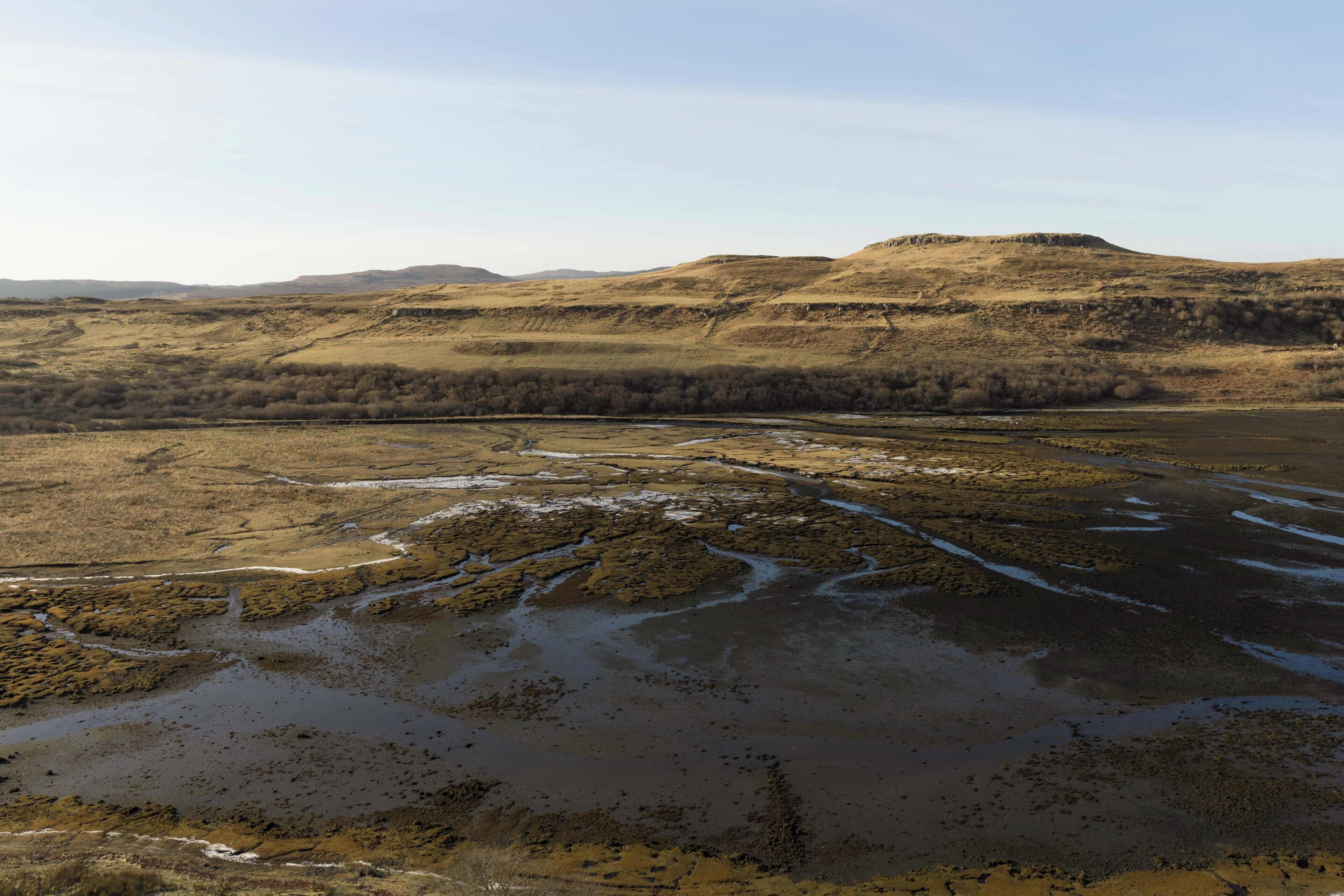 Een uitgestrekt landschap met een rivier die door een vallei kronkelt, omgeven door glooiende heuvels.