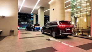 Ein Parkplatz mit einem schwarzen SUV und einem blauen SUV, ein Gebäude mit Glasfassade und einer Sitzgelegenheit.