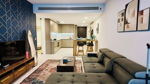 A modern living room with a sofa, TV, and a coffee table. There is a kitchen in the background with a dining area. - Eaton Residence KLCC - JD Home Stay | Two Bedroom Apartment with KLCC view (Kuala Lumpur)