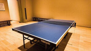 Ein Tischtennis-Tisch mit Netz in einem Raum mit Holzboden und einer Bank.