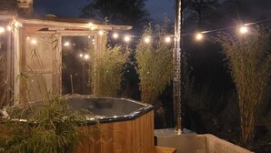 An outdoor hot tub area with a wooden structure, surrounded by plants and a string of lights.