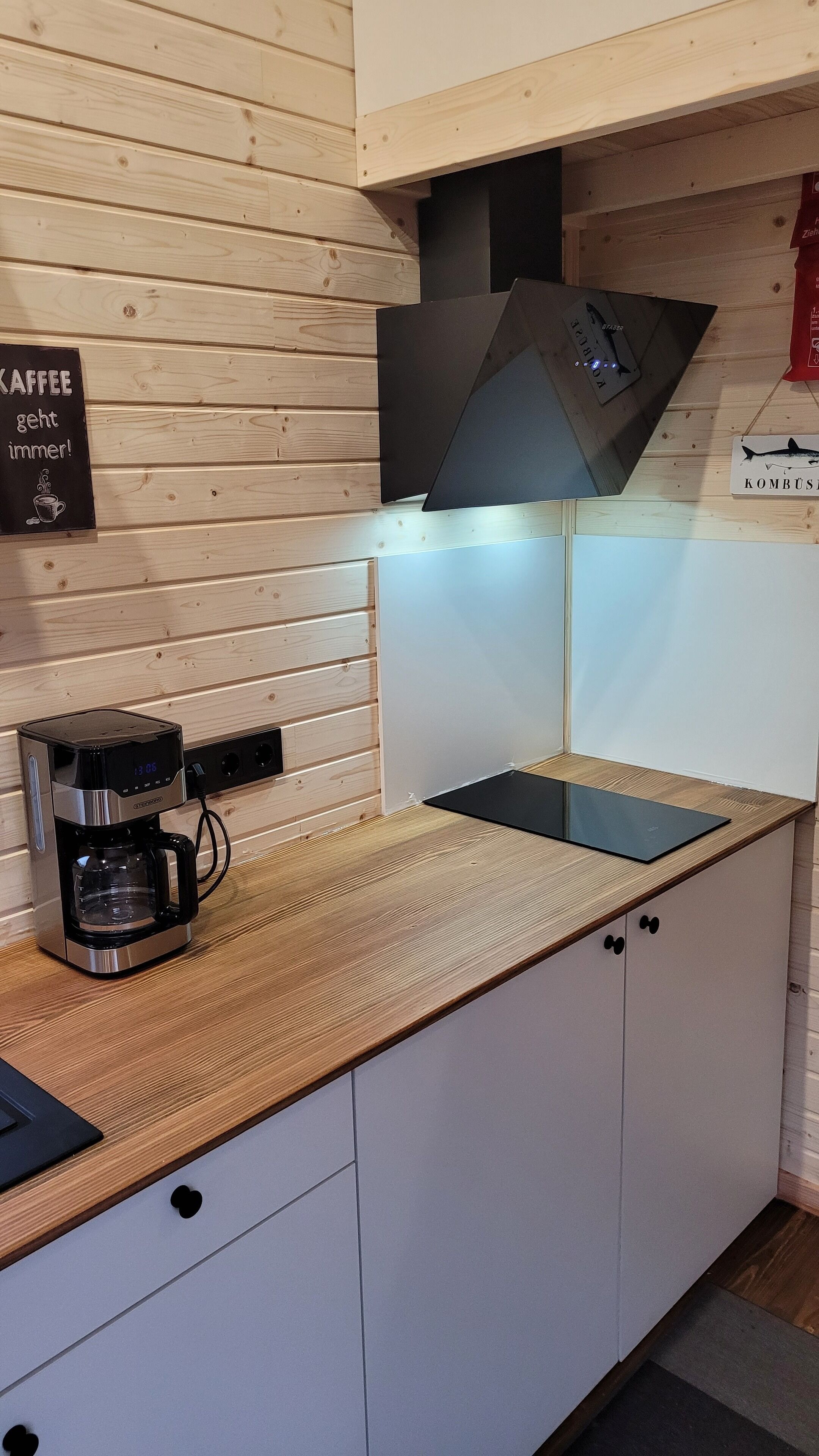 Eine kleine Küche mit Kaffeemaschine, schwarzer Arbeitsplatte und Holzschränken.