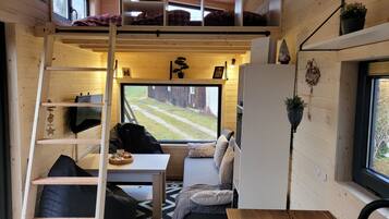 Interior acogedor de una cabaña con cama abuhardillada, comedor y un ventanal con vistas al jardín.